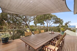 Une terrasse extérieure avec une table et des chaises en bois, entourée de plantes en pot et d’un grand auvent.