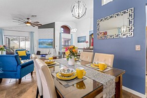 Un coin repas avec une table dressée pour quatre personnes, un canapé bleu et un ventilateur de plafond.