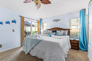 Une chambre avec un grand lit, un ventilateur de plafond, une table de chevet et une fenêtre avec des rideaux.