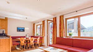 En moderne stue med spiseområde i træ, rød sofa og store vinduer.