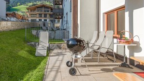 En terrasse med grill, udendørs møbler og udsigt til et bjerglandskab.