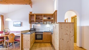 Cocina compacta con armarios de madera, horno empotrado y comedor con mesa y sillas.