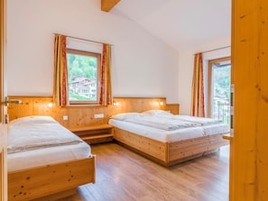 A room with two wooden beds, wooden walls, and windows with curtains.
