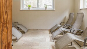 Un área de espera con varias sillas acolchadas, una ventana con plantas en macetas y suelo de baldosas.