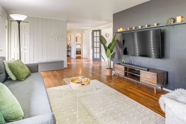 A modern living room with a grey sofa, a large flat-screen TV, a wooden entertainment unit, and a potted plant. - Pregame Pool Matches, 1 Mi to UO Campus (Eugene)