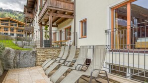A terrace with lounge chairs, a stone wall, and a view of a mountain.