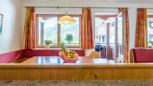 A dining area with a wooden table, red cushioned bench, and a fruit basket.