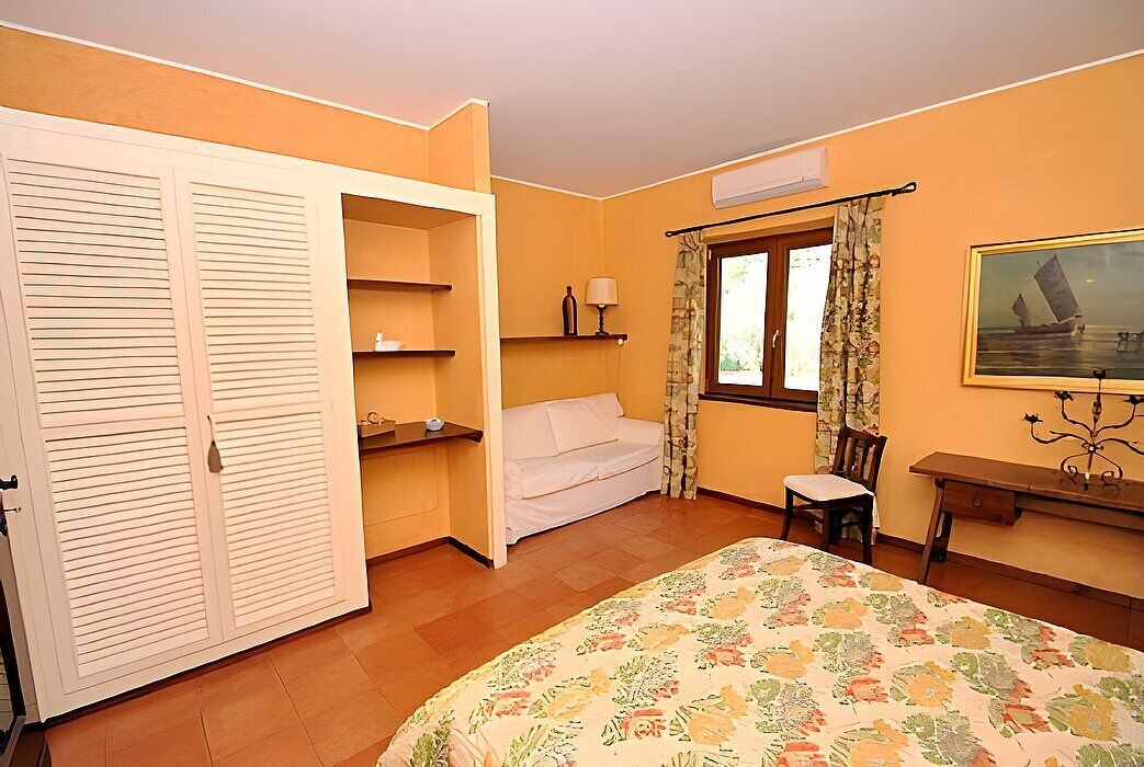 A bedroom with a bed, a chair, a desk, a wardrobe, and a window with curtains.