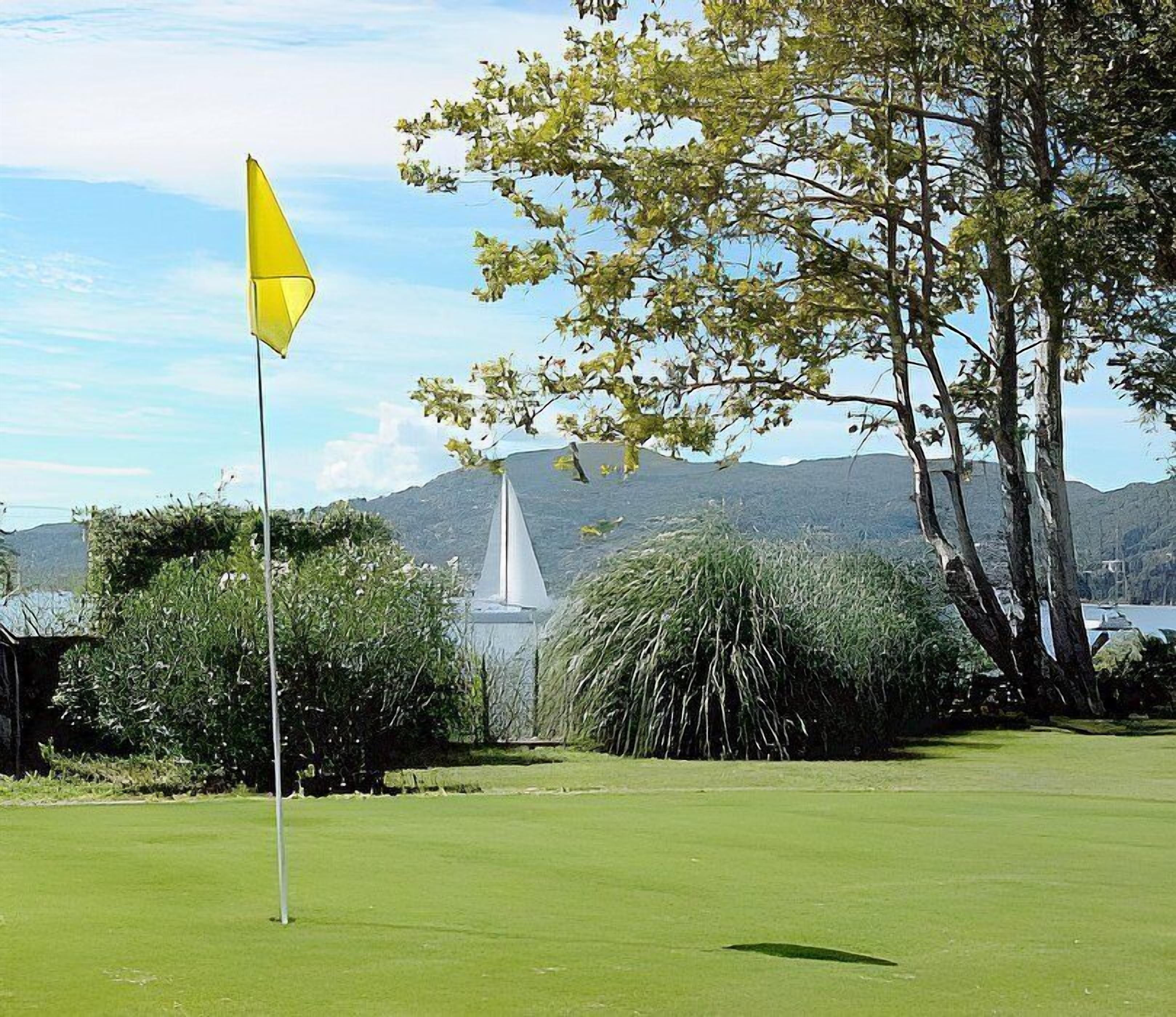 A golf course with a flagstick, a fountain, and a mountainous backdrop.