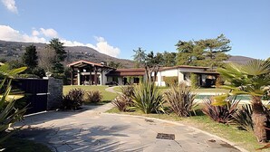 A modern house with a stone pathway leading to the entrance, surrounded by tropical plants and a mountain in the background.