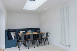A dining area with a wooden table and four chairs, a blue bench with cushions, and a skylight above. - Spacious House, Private Parking & Garden (Gloucestershire)