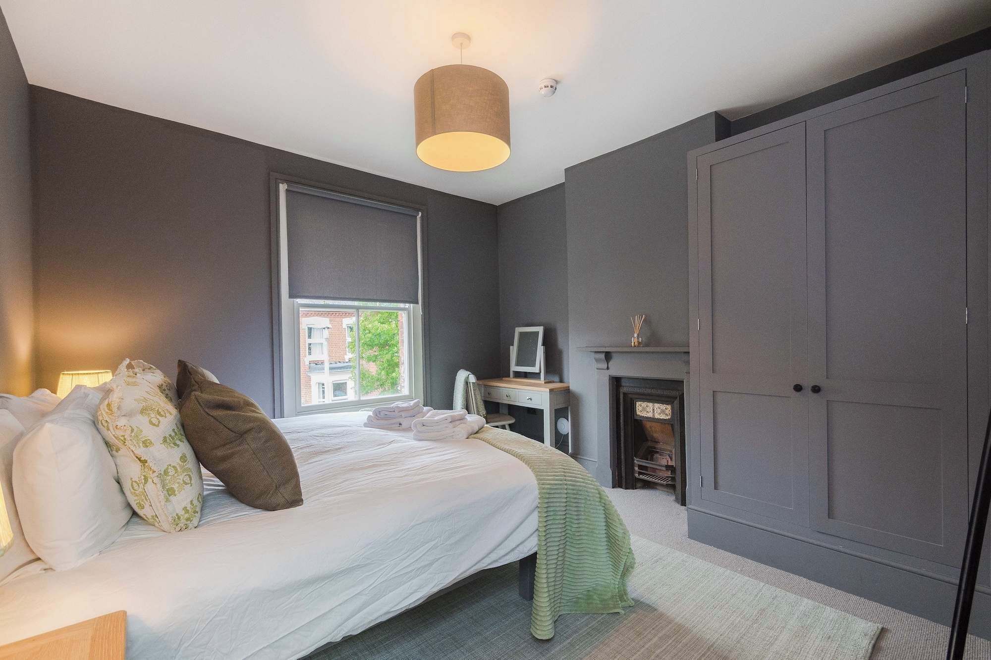 A bedroom with a bed, a desk, a fireplace, and a wardrobe.