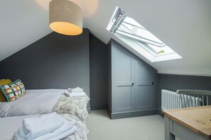 A bedroom with a sloped ceiling, a skylight, a bed with pillows, a radiator, and a wooden table. - Spacious House, Private Parking & Garden (Gloucestershire)