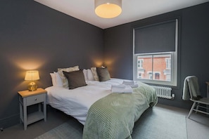 Camera da letto con un letto, comodino, lampada, finestra, termosifone e vista sugli edifici.