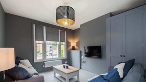 A modern living room with a grey sofa, a white coffee table, and a TV mounted on the wall. - Spacious House, Private Parking & Garden (Gloucestershire)
