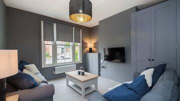 A modern living room with a grey sofa, a white coffee table, and a TV mounted on the wall.