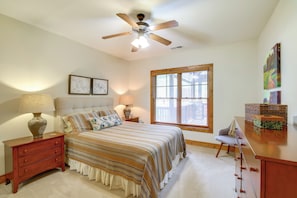 Quarto com cama, mesas de cabeceira, cômoda, ventilador de teto e janela com persianas.