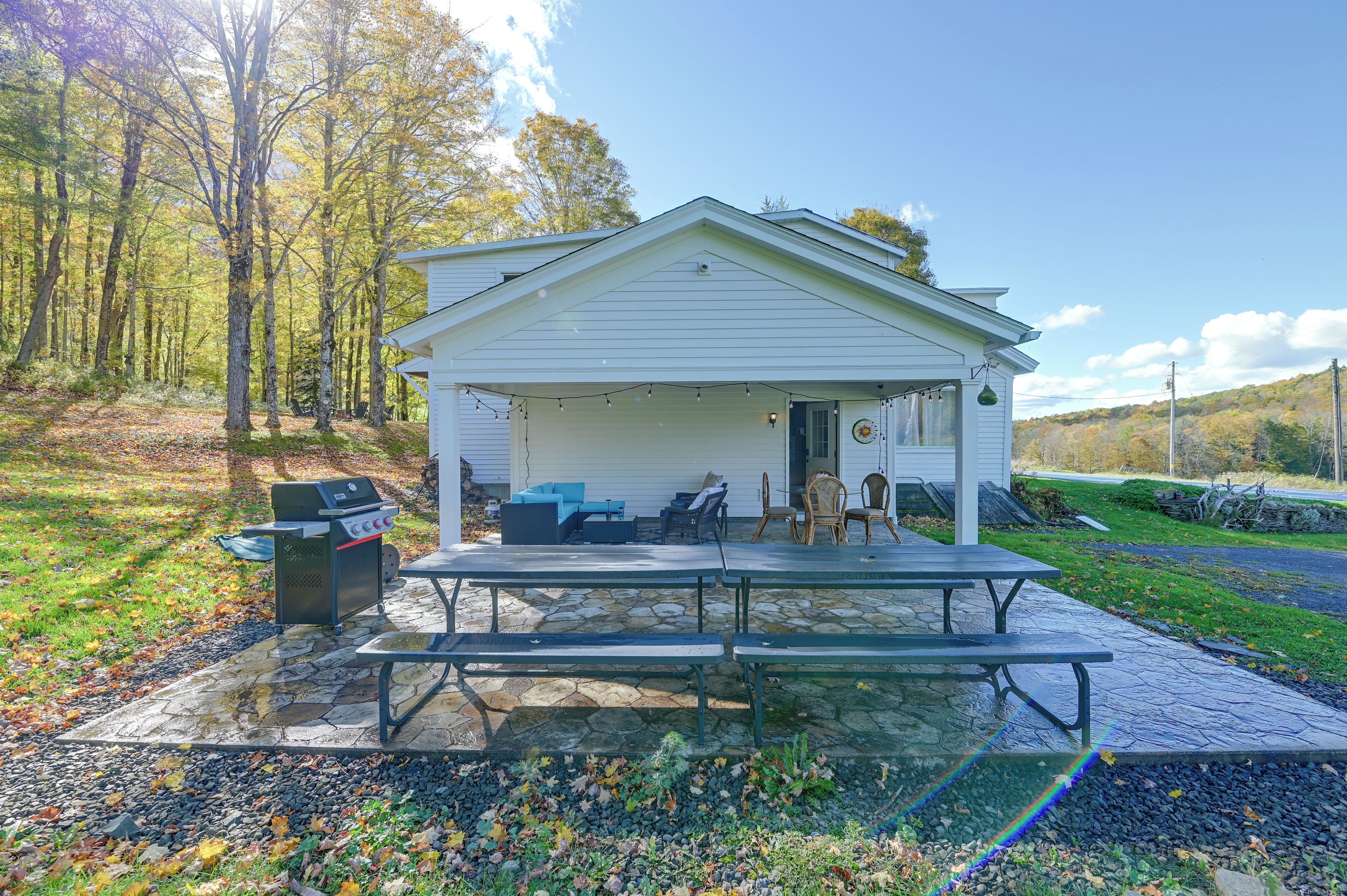 A covered outdoor area with a picnic table, barbecue grill, and seating.