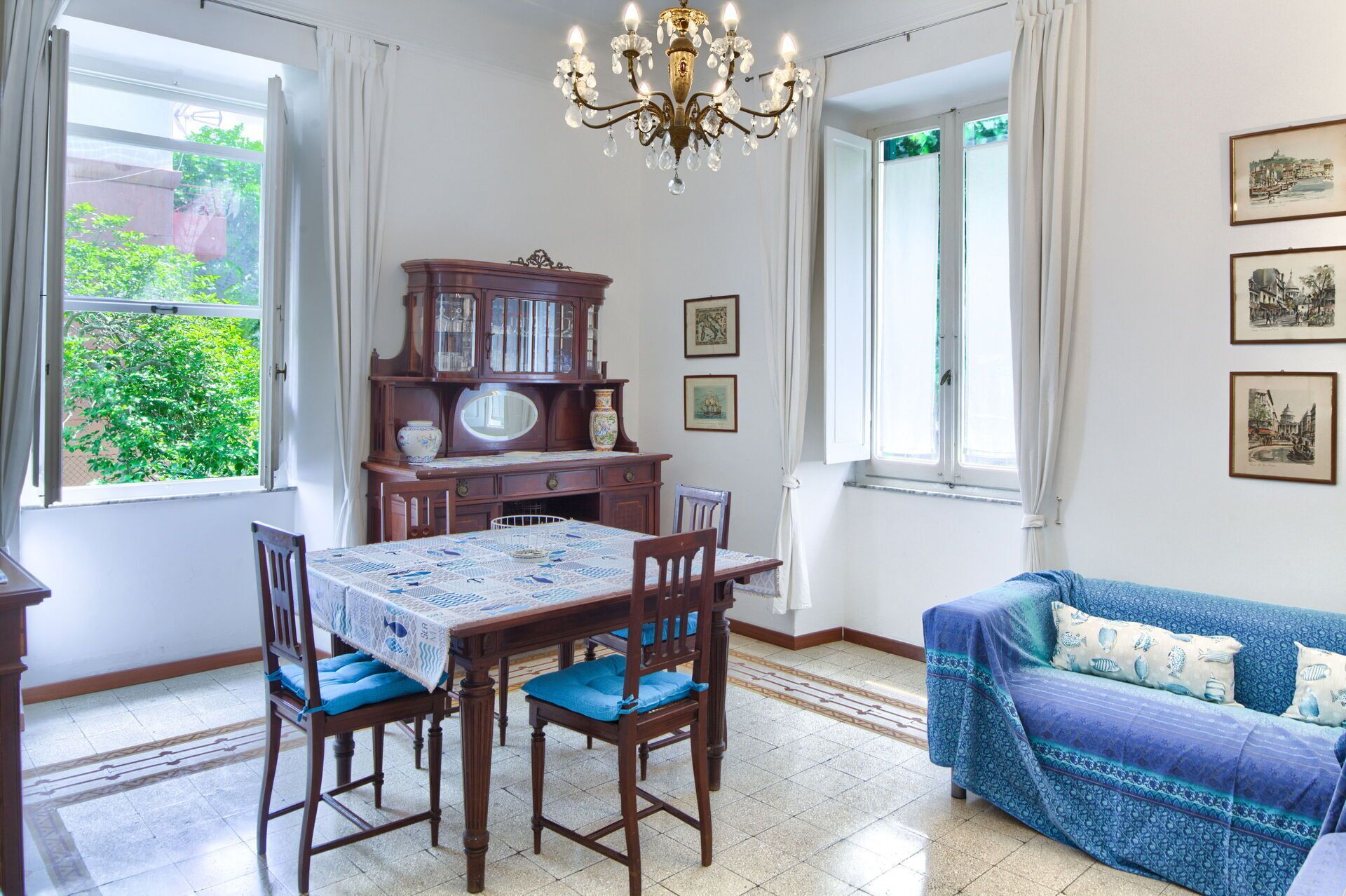 Zona pranzo con tavolo e sedie in legno, un lampadario e un divano blu con cuscini decorati.