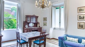 A dining area with a wooden table and chairs, a chandelier, and a blue sofa with patterned cushions. - Spacious apartment with garden, near the beach (Levanto)