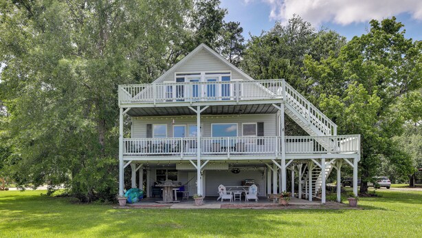 A two-story house with a balcony, a covered porch, and a small outdoor seating area with a table and chairs. - Spacious Riverfront Cottage w/ Dock in Green Pond! (Green Pond)