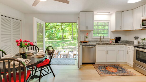 A modern kitchen with white cabinets, a stainless steel dishwasher, and a large window overlooking a garden. - Walk to Lake Munson: Tree-Filled Tallahassee Gem! (Tallahassee)