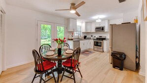A modern kitchen with white cabinets, a dining area with a round table and chairs, and a ceiling fan. - Walk to Lake Munson: Tree-Filled Tallahassee Gem! (Tallahassee)