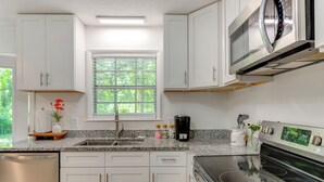 A modern kitchen with white cabinets, a granite countertop, a stainless steel refrigerator, and a built-in oven. - Walk to Lake Munson: Tree-Filled Tallahassee Gem! (Tallahassee)