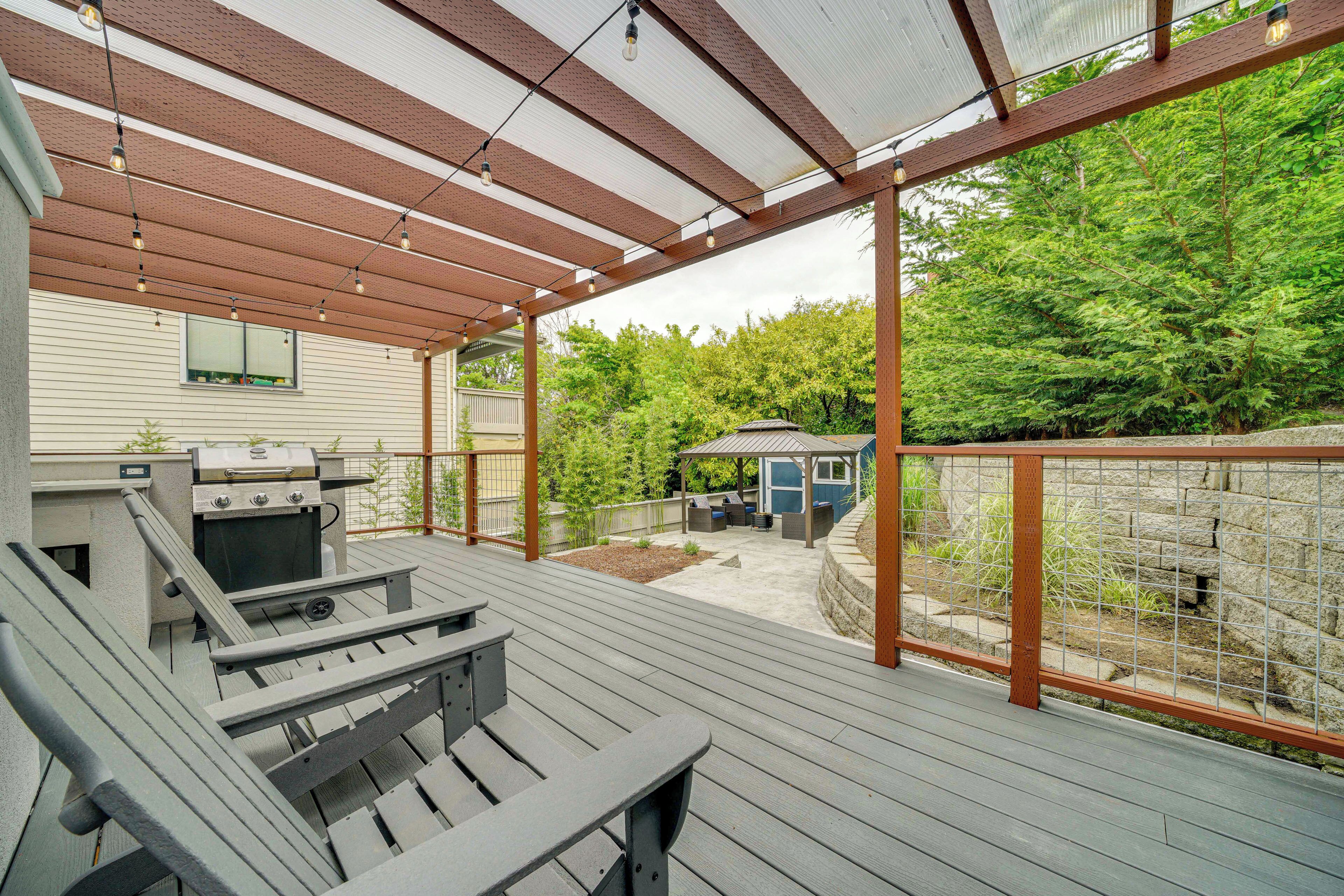 Überdachte Terrasse im Freien mit Grill, Sitzgelegenheiten und Blick auf ein bewaldetes Gebiet.