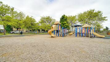 Un parque infantil con toboganes y estructuras para escalar, rodeado de árboles y un suelo de grava.