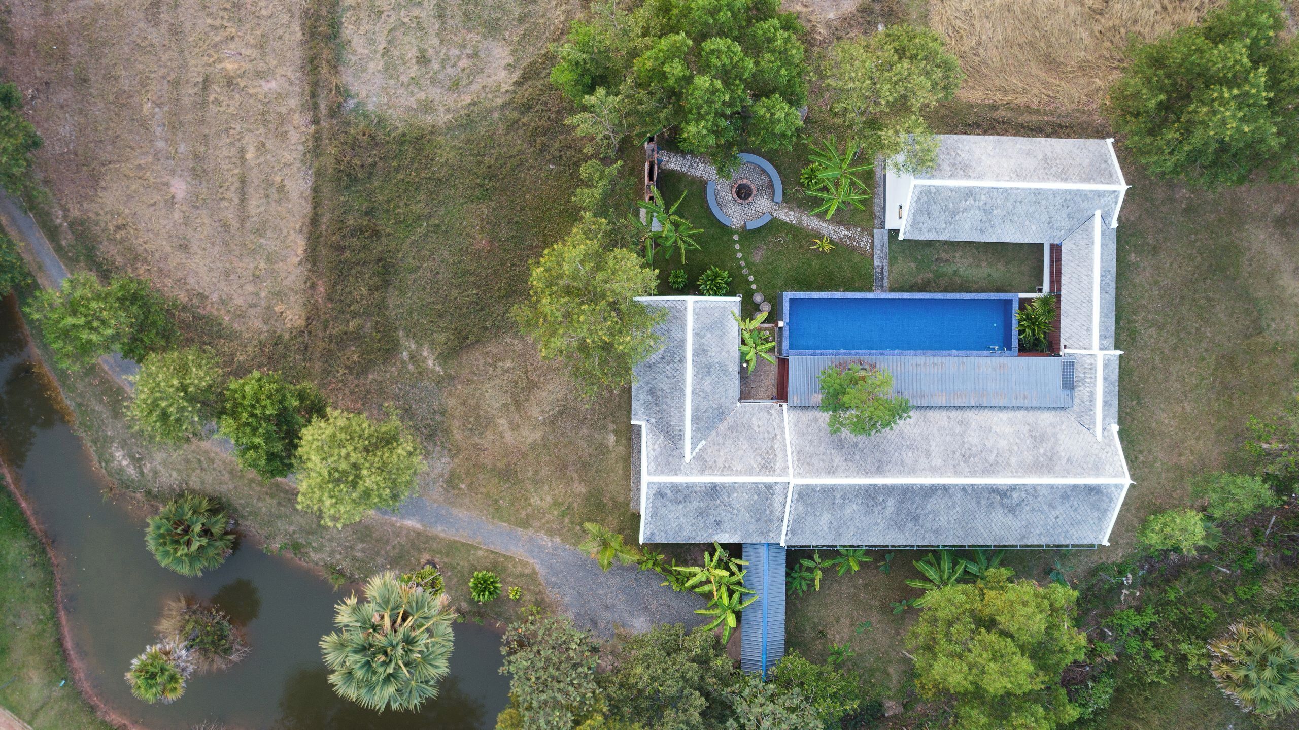 An aerial view of a house with a swimming pool, surrounded by trees and a small garden.