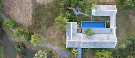 An aerial view of a house with a swimming pool, surrounded by trees and a small garden.