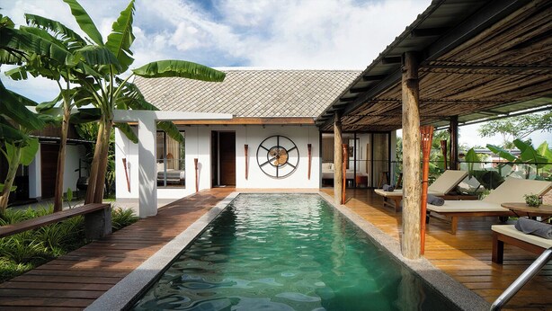 A pool area with a wooden deck, lounge chairs, and a building with a tiled roof. - Sré Lodge Living Style Community (Kampot)