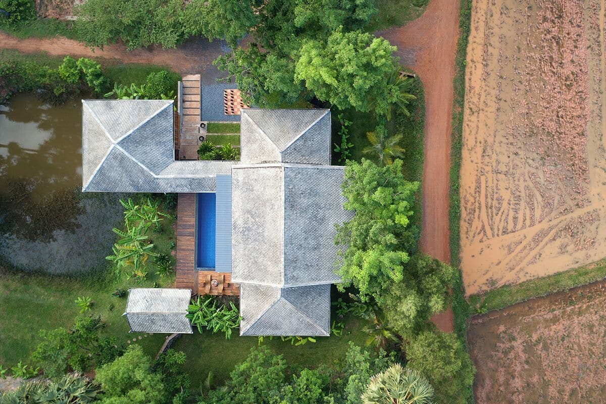 An aerial view of a modern house with a central courtyard, surrounded by lush greenery and a body of water.