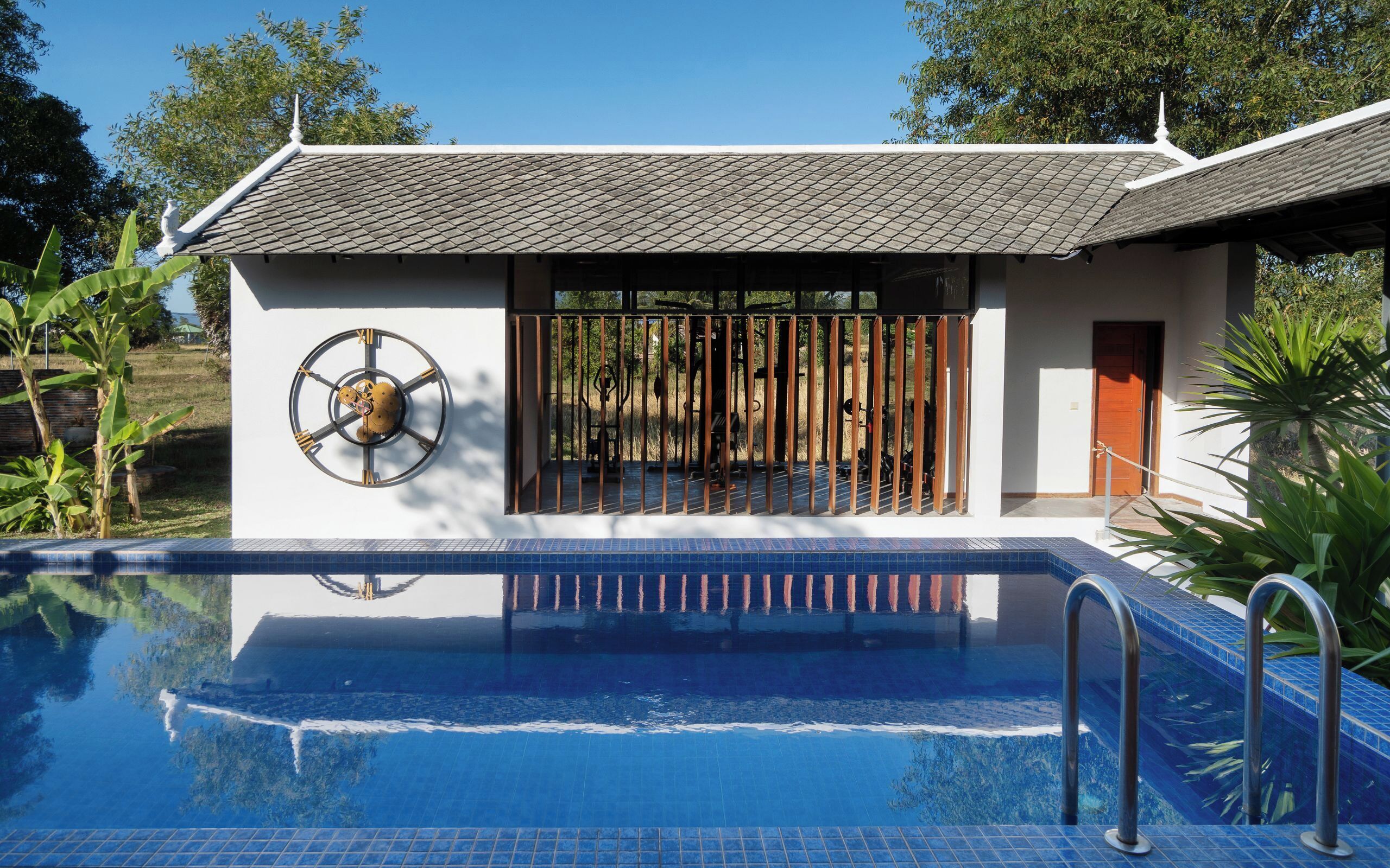 A modern building with a swimming pool, a large clock on the wall, and a gated entrance.