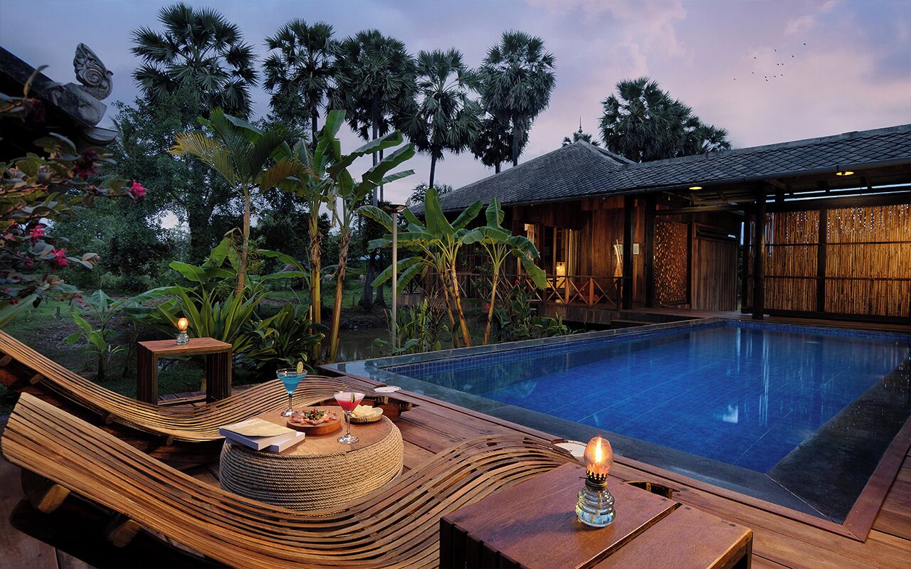 A poolside area with a wooden deck, lounge chairs, and a small table with a candle.