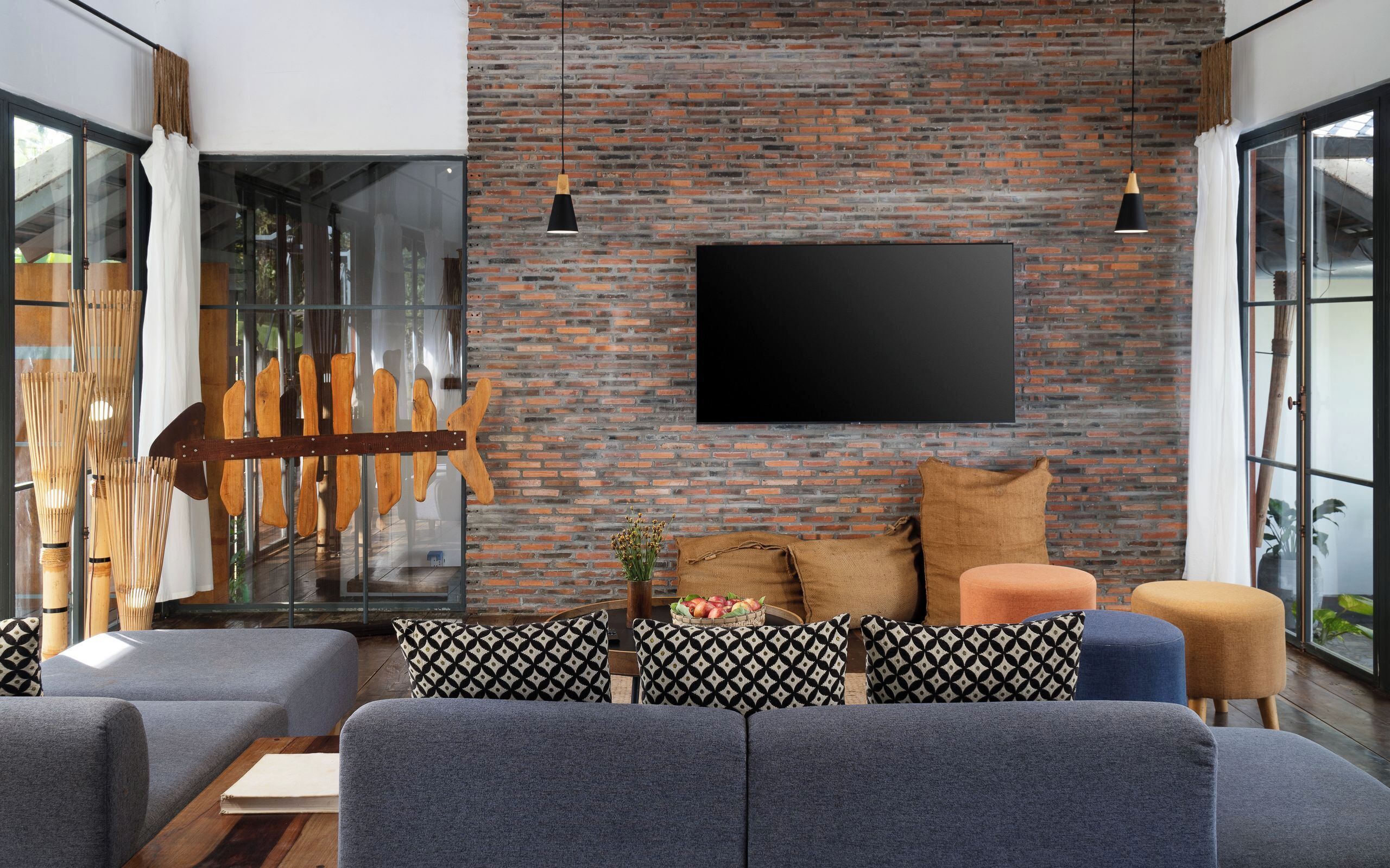 A modern living room with a brick wall, a mounted TV, and a glass door leading outside.