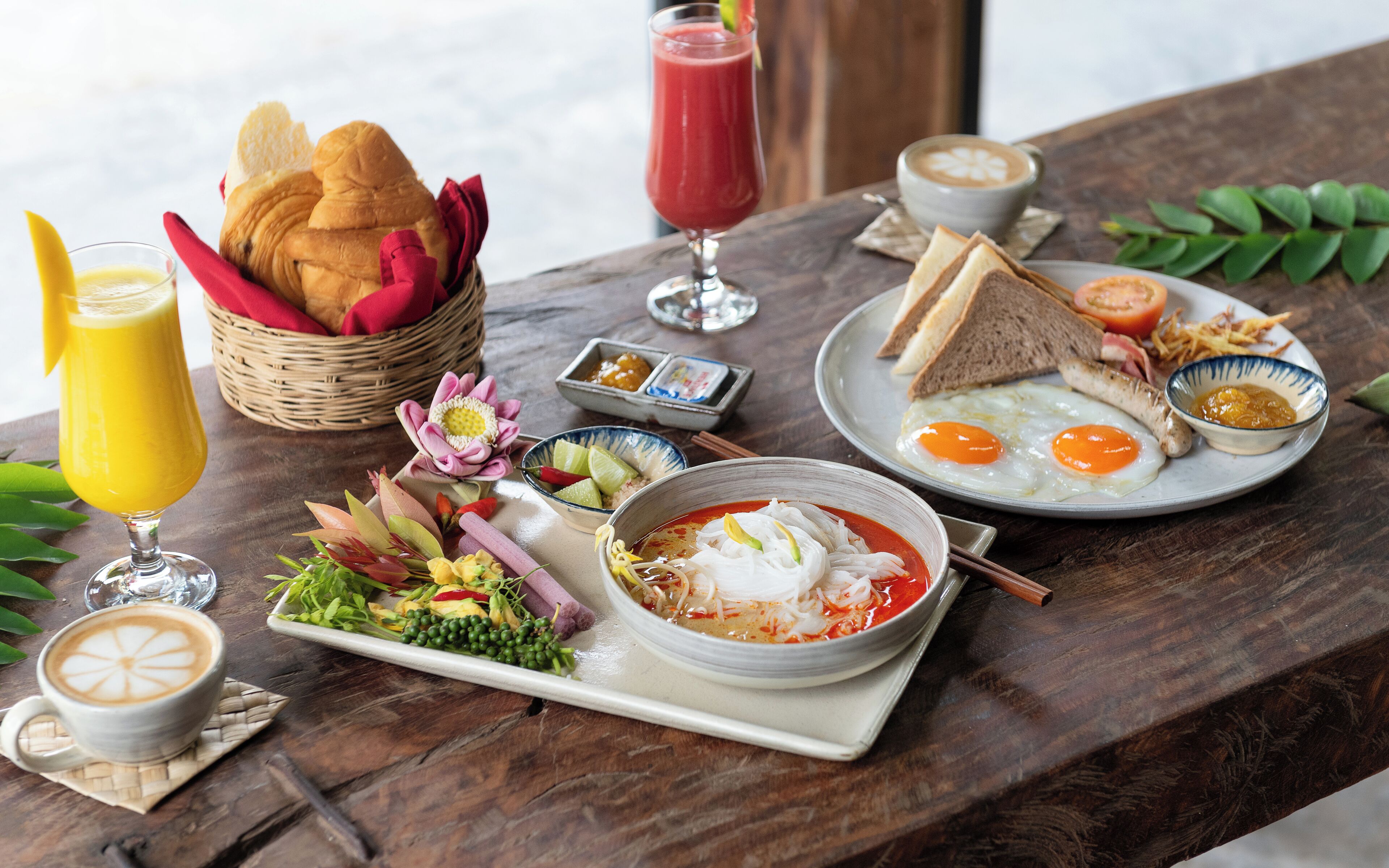 A breakfast setting with a variety of dishes including eggs, toast, and soup, along with drinks and a basket of bread.