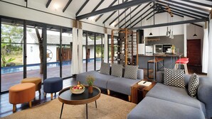 A modern interior with a sofa set, a round table with fruit, and a kitchen area. - Sré Lodge Living Style Community (Kampot)