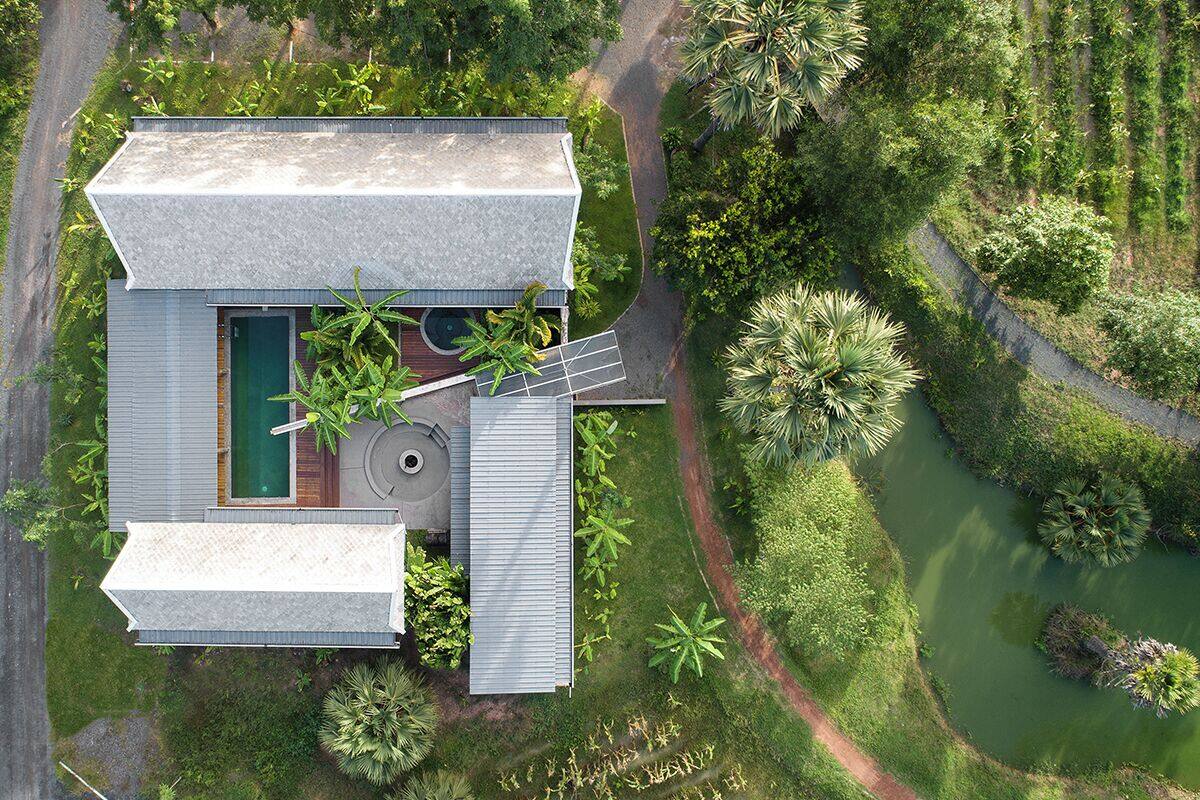 An aerial view of a modern house with a swimming pool, surrounded by lush greenery and a small pond.