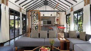 Una sala moderna con un conjunto de sofás, una mesa de centro con fruta, y una zona de cocina con bodegas.