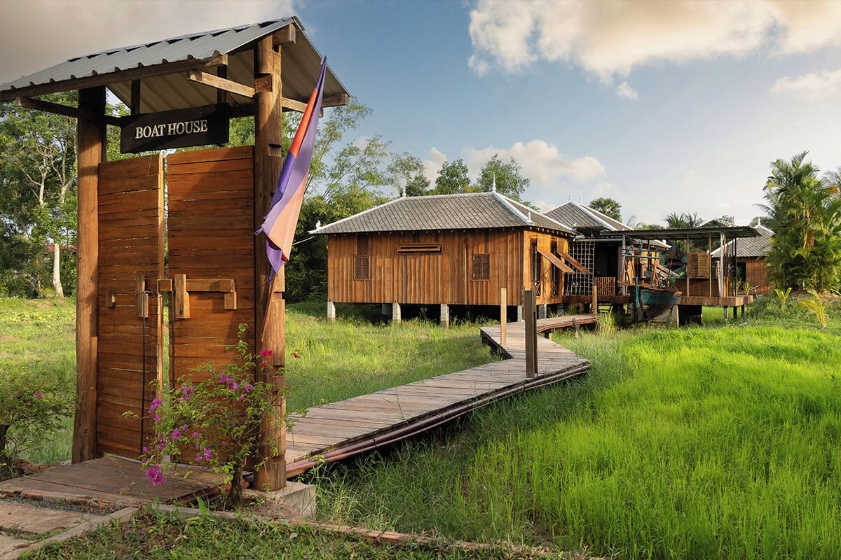 A wooden boat house with a sign, surrounded by lush greenery and palm trees.