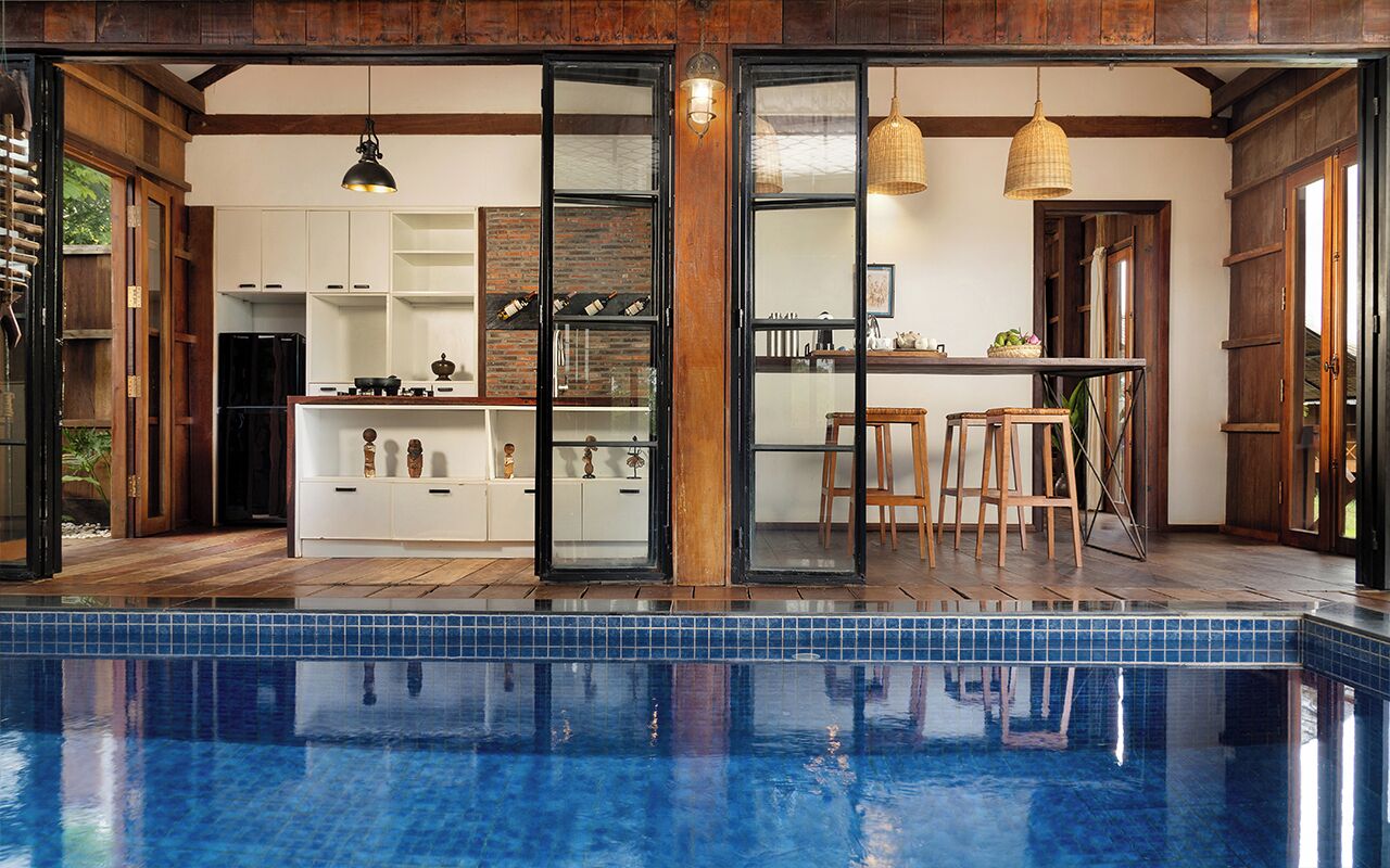 A modern kitchen with a glass door leading to a dining area, a pool, and wooden flooring.