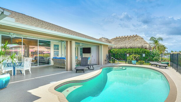 A swimming pool with lounge chairs, a covered patio, and a thatched-roof structure. - Dock & Lanai! Waterfront Oasis Near Boca Grande (Port Charlotte)