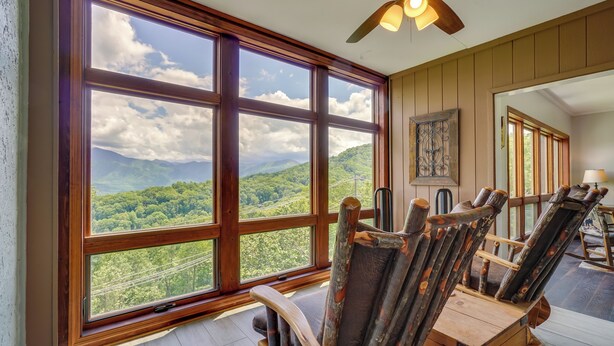 Habitación con amplias ventanas que ofrecen vistas a un paisaje montañoso. Se observan sillas de madera y un ventilador de techo.