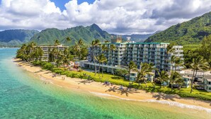 A beachfront hotel with multiple floors, a pool area, and a view of the ocean and mountains. - Oceanfront Condo: Stunning Sunrise & Ocean Views (Hauula)