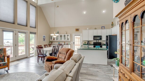 A spacious living area with a large sofa, dining table, and chairs. There is a kitchen with white cabinets and a refrigerator. - Deck & Views: Lake Murray Escape in Chapin! (Chapin)