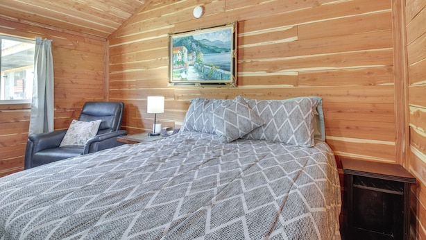 Una habitación acogedora de madera con una cama, una silla y un cuadro en la pared.