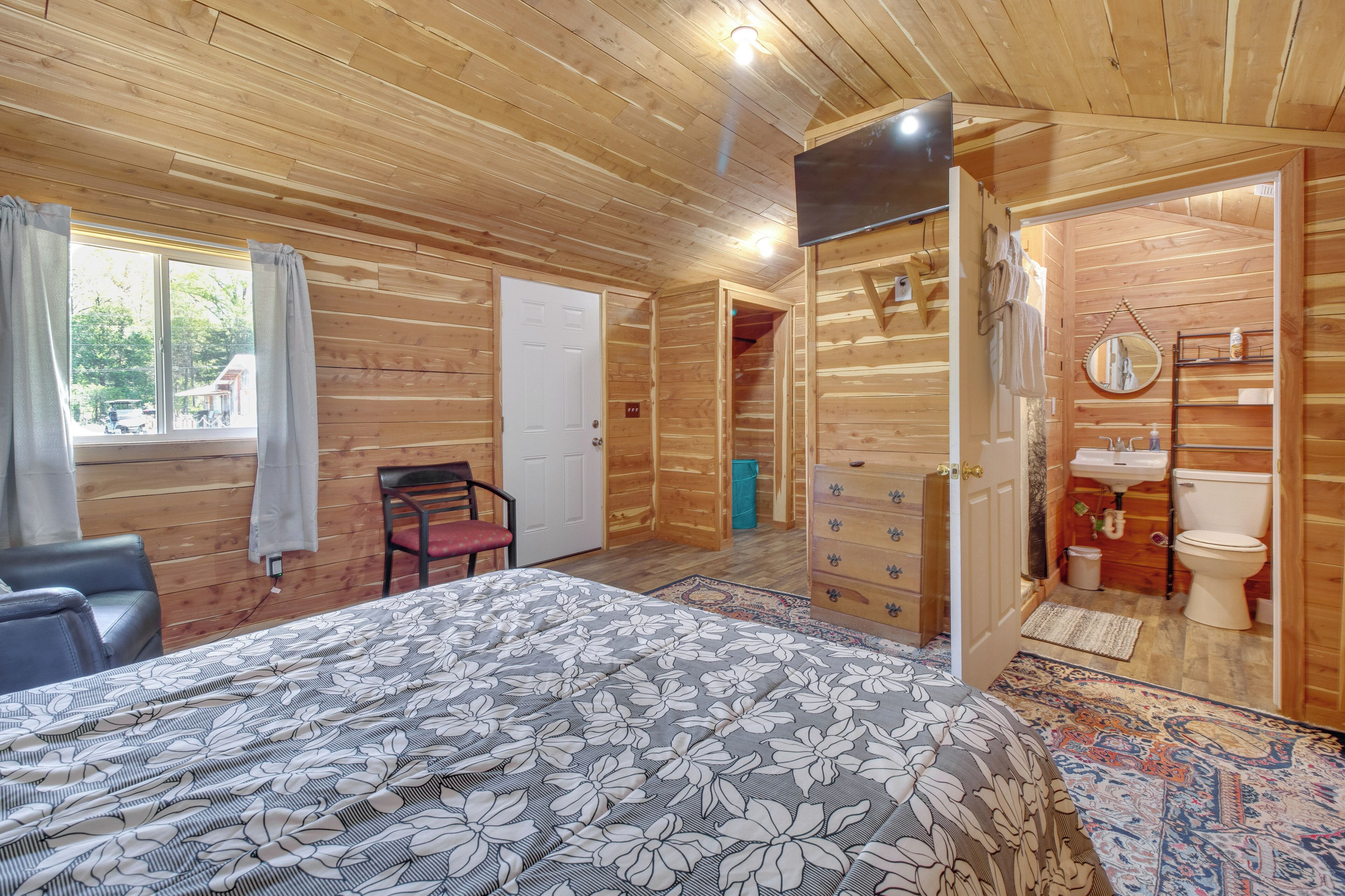 Een slaapkamer in een houten hutje, met een bed, een stoel, een kledingkast en een zichtbare badkamer door een geopende deur.