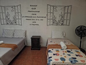 Una habitación con dos camas, una mesita, un reloj de pared y un ventilador.